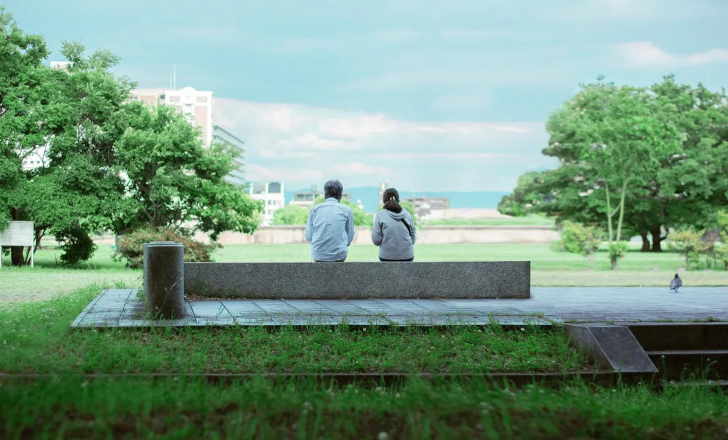 Two people sitting on a bench looking out at the ocean.