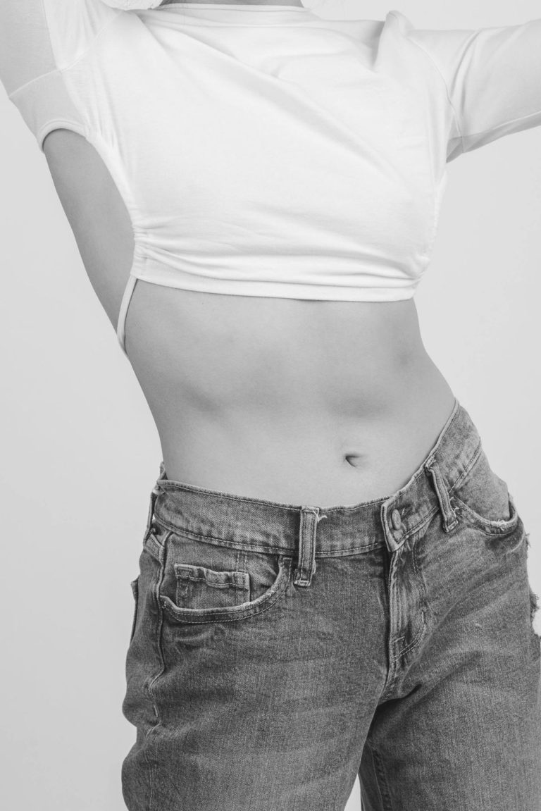 A woman in white shirt and jeans with her stomach exposed.