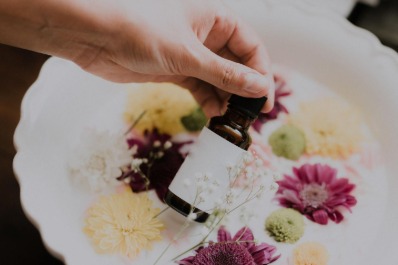 A person holding an oil bottle in front of flowers.