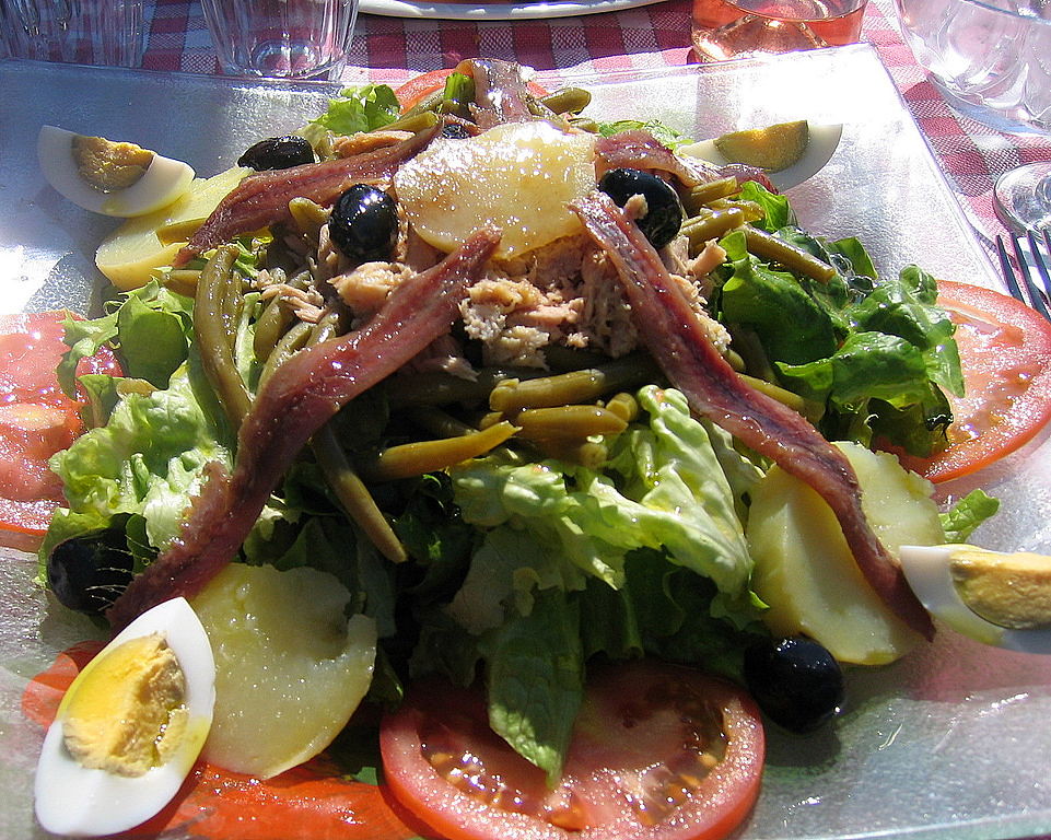 A salad with tomatoes, olives and bacon on top.